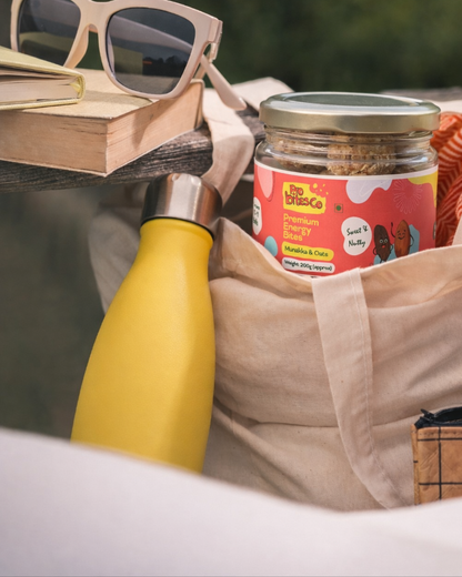 Pro Bites Co Munakka Badam Oats jar in a tote bag with a water bottle and sunglasses